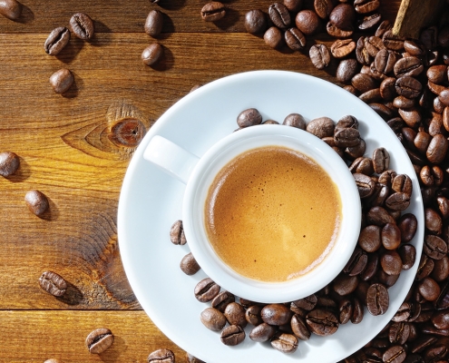 cup of coffee with scattered whole coffee beans on wood table